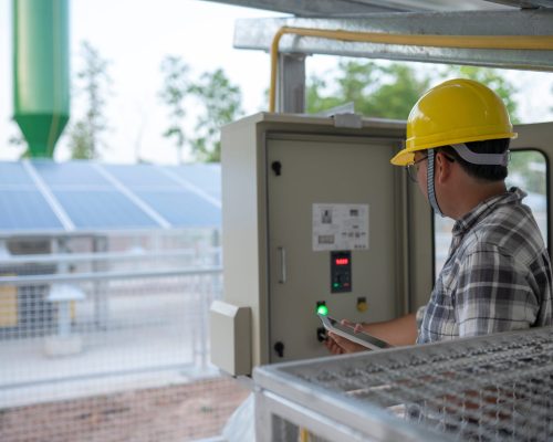 Technician at groundwater pumping station with solar or alternative energy uses a tablet to control and monitor.