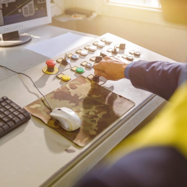 Close up of man factory worker sitting at the table with desktop computer and turning key on control panel